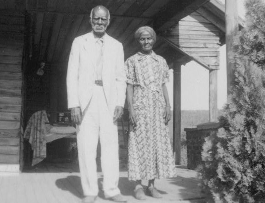 Anderson and Minerva Edwards, an elderly couple, on the side porch of a house, in sunlight. 